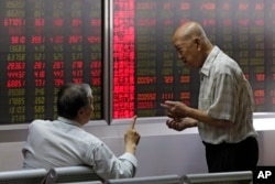 FILE - People chat as they monitor stock prices at a brokerage house in Beijing, Aug. 16, 2018.