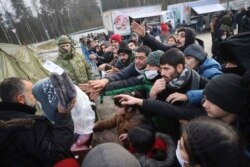Para migran menerima pembagian pakaian hangat ketika musim dingin mulai melanda kota Grodno, Belarus dekat perbatasan Polandia (28/11).