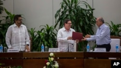 Cuba's Foreign Minister Bruno Rodriguez, center, gives a copy of the peace accord to Humberto de La Calle, right, head of Colombia's government peace negotiation team, as Ivan Marquez, left, chief negotiator of the Revolutionary Armed Forces of Colombia, or FARC, watches, after the signing of the latest text of the peace accord between the two sides in Havana, Cuba, Nov. 12, 2016.