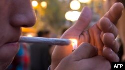 FILE - A young man lights a marijuana cigarette during a demonstration demanding a new law on cannabis in Montevideo, May 8, 2013.