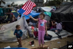 Seven-year-old Honduran migrant Genesis Belen Mejia Flores waves an American flag at U.S. border control helicopters flying overhead near the Benito Juarez Sports Center serving as a temporary shelter for Central American migrants, in Tijuana, Mexico, Nov