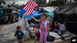 Honduran migrant Genesis Belen Mejia Flores, 7, waves an American flag at U.S. border control helicopters flying overhead near the Benito Juarez Sports Center serving as a temporary shelter for Central American migrants, in Tijuana, Mexico, Nov. 24, 2018.