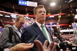 FILE - Then-Trump campaign chairman Paul Manafort talks to reporters on the floor of the Republican National Convention, in Cleveland, Ohio, July 17, 2016. Rick Gates is seen in the background (left).