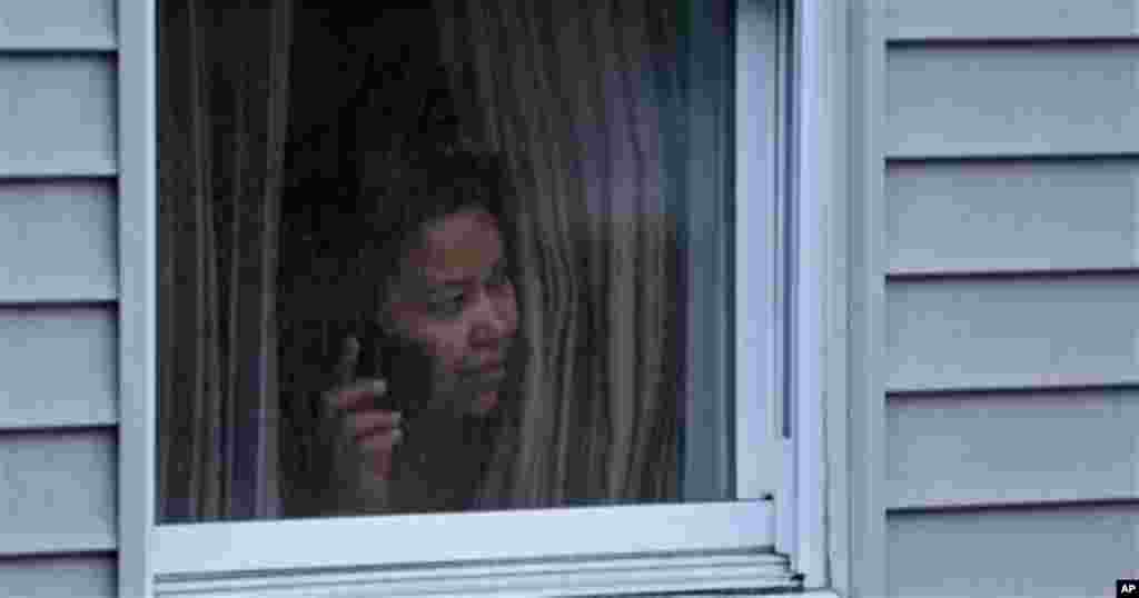 A woman looks out a window at her home as police start to search an apartment building while looking for a suspect in the Boston Marathon bombings in Watertown, Mass., Friday, April 19, 2013. 