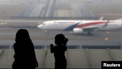 FILE - A woman and a girl look at a Malaysia Airlines plane on the tarmac of Kuala Lumpur International Airport.
