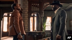 This image released by Netflix shows Jonathan Majors, left, and Idris Elba in a scene from 'The Harder They Fall.' (David Lee via AP)