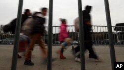 FILE - Refugees and migrants are seen walking behind a fence at the border between Slovenia and Austria at Spielfeld, Austria, Feb. 16, 2016. 