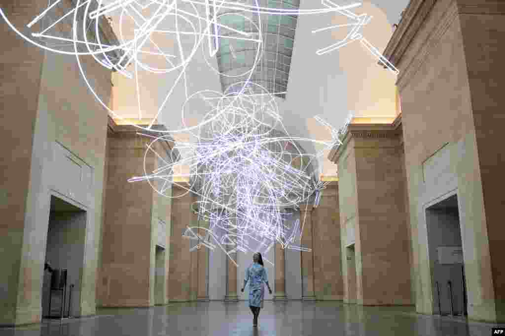 A gallery assistant poses for photographers during a photocall to promote Welsh artist&#39;s Cerith Wyn Evans new light installation entitled &quot;Forms in Space... by Light (in Time)&quot;, made up of nearly 2km of neon lights, at Tate Britain in London.