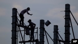 FILE - Workers on scaffolding are silhouetted at a construction site near Phnom Penh, Cambodia.