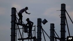 FILE - Workers on scaffolding are silhouetted at a construction site near Phnom Penh, Cambodia, March 21, 2017. Despite a growing economy, Cambodian construction workers earn as little as $2.50 a day.