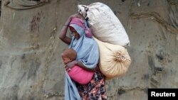 A displaced Somali woman carries a child and her belongings after fleeing famine in the Marka Lower Shebbele regions, as she arrives at a temporary dwelling in the capital Mogadishu.