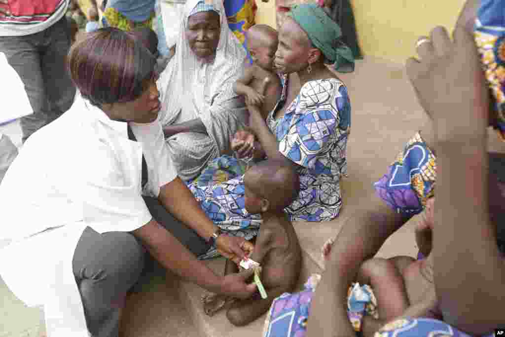 Seorang dokter memeriksa seorang anak yang kurang gizi sementara para perempuan dan anak-anak yang diselamatkan oleh tentara Nigeria menunggu giliran pemeriksaan di kamp pengungsi di Yola, Nigeria, setelah diselamatkan dari tawanan Boko Haram (3/5).