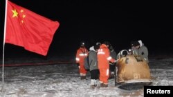 Researchers work around Chang'e-5 lunar return capsule carrying moon samples next to a Chinese national flag, after it landed in northern China's Inner Mongolia Autonomous Region, December 17, 2020. (China Daily via REUTERS)