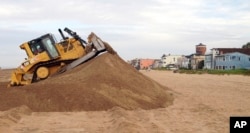 FILE - In this Oct. 28, 2015, photo, a bulldozer piles sand into a high berm to protect homes along Sunset Beach in Huntington Beach, California.