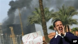 An Egyptian protester chant anti-government slogans, as another holds a sign in Arabic reading 'Voice of the People, no to Mubarak,' as smoke billows from the National Council for Women and Children's building, in downtown Cairo, January 29, 2011