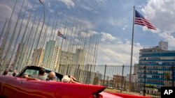 FILE - Tourists ride a vintage American convertible as they drive next to the American flag and a Cuban flag at the United States embassy in Havana, Cuba, March 18, 2016.