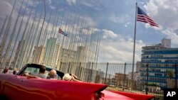 FILE - Tourists ride in a vintage American convertible as they drive next to the American flag and a Cuban flag at the U.S. Embassy in Havana, Cuba, March 18, 2016.