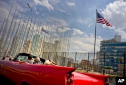 FILE - Tourists ride a vintage American convertible as they drive next to the American flag and a Cuban flag at the United States embassy in Havana, Cuba, March 18, 2016.