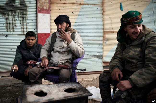 U.S.-backed Syrian Democratic Forces (SDF) fighters sit outside a building as fight against Islamic State militants continue in the village of Baghouz, Syria, Feb. 16, 2019.