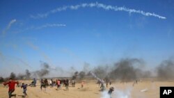 Demonstran melarikan diri dan berlindung dari gas air mata yang ditembakkan oleh pasukan Israel dekat pagar perbatasan Jalur Gaza dan Israel, saat protes di Khan Younis, Jumat, 17 Agustus 2018.