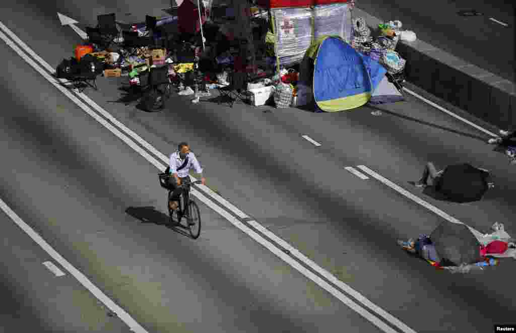 A man rides his bicycle to work along an area blocked by protesters at the main street to the financial Central district outside of the government headquarters building in Hong Kong, Oct. 6, 2014. 