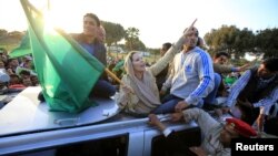 Aisha Gaddafi, daughter of Libya's leader Muammar Gaddafi, holds a Libyan flag as she greets supporters at Bab Al-Aziziyah in Tripoli March 19, 2011. Thousands of Libyans packed into Muammar Gaddafi's heavily fortified Tripoli compound on Saturday to form