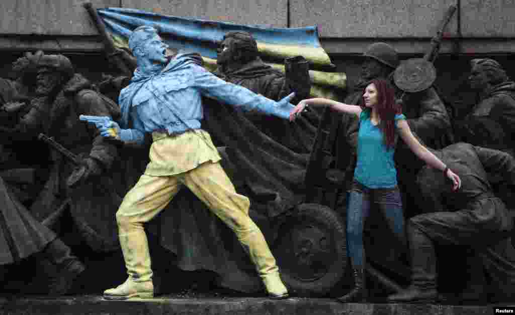 A woman poses for a photo at the base of the Soviet Army monument in Sofia, Bulgaria, parts of which have been painted in the colors of the Ukranian flag by an unknown person, Feb. 23, 2014.