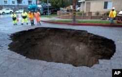 Inspectors examine a sinkhole in Studio City, north of Los Angeles, Feb. 18, 2017. Two vehicles fell into the 20-foot sinkhole on Friday night and firefighters had to rescue one woman who escaped her car but was found standing on her overturned vehicle.