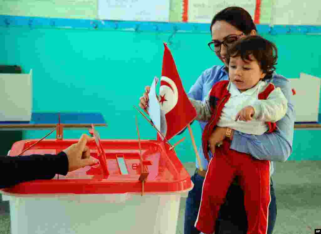 A woman casts her vote while holding her child, during the first round of the Tunisian presidential election, in a polling station at Marsa, outside Tunis, Nov. 23, 2014.