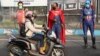 Petugas kepolisian mengenakan kostum superhero menyemprotkan disinfektan kepada para pengendara motor di Pasuruan, Jawa Timur, 9 April 2020. (Foto: AP)