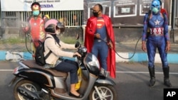 Petugas kepolisian mengenakan kostum superhero menyemprotkan disinfektan kepada para pengendara motor di Pasuruan, Jawa Timur, 9 April 2020. (Foto: AP)