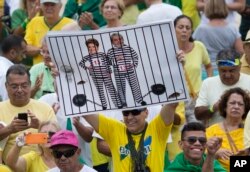 FILE - A demonstrator holds a poster with the photo of Brazilian president Dilma Rousseff and former President Luiz Inacio Lula da Silva in prison stripes during a protest on Copacabana beach in Rio de Janeiro, Brazil, March 13, 2016.