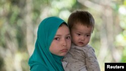 FILE - A suspected Uighur from China's troubled far-western region of Xinjiang, holds an infant as they rest inside a temporary shelter on March 14. They were detained at the immigration regional headquarters near Thailand-Malaysia border.