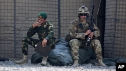 FILE - In this Aug. 5, 2015 photo, an Afghan National Army soldier, left, smokes as a U.S. Army soldier from Charlie Company, 2-14 Infantry Regiment, 2nd Brigade, 10th Mountain Division sits next to him in Camp Khogyani in Nangarhar province, east of Kabul, Afghanistan.