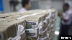 FILE - Stacks of Myanmar kyat are seen on the counter before a client collects them, at a bank in Yangon, Myanmar, Oct. 19, 2015.