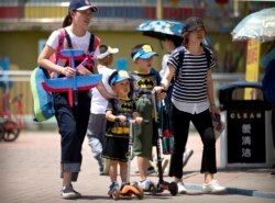 Dua perempuan berjalan dengan anak-anak mengenakan pakaian yang serasi di taman umum pada Hari Anak Internasional di Beijing. (Foto: AP/Mark Schiefelbein)