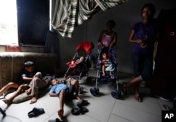 En esta foto del 27 de junio de 2018, algunas madres vigilan a niños venezolanos mientras otros trabajan, dentro de una casa escasamente amueblada compartida por unas 10 personas en Cúcuta, Colombia.