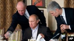 FILE - In this Nov. 11, 2011, photo, businessman Yevgeny Prigozhin, left, serves food to Russian Prime Minister Vladimir Putin, center, during dinner at Prigozhin's restaurant outside Moscow, Russia. 