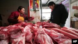 A customer, right, looks at meat at a shop in Shanghai, China, Jan. 17, 2012.