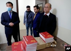 Chinese lecturer, Zhiwei Hu, left, teachers and officials of the Chinese Language Department stand in front of Chinese language books intended for students in Salahaddin University in Irbil, Iraq, Jan. 19, 2021.