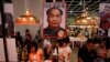 FILE - Book lovers read beneath poster promoting "Stange Leung Chun-ying," which depicts the new Hong Kong Chief Executive as the late Chinese leader Mao Zedong, Hong Kong Book Fair, July 18, 2012.