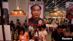 FILE - Book lovers read beneath poster promoting "Stange Leung Chun-ying," which depicts the new Hong Kong Chief Executive as the late Chinese leader Mao Zedong, Hong Kong Book Fair, July 18, 2012.