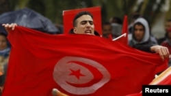 A demonstrator holds a Tunisian flag as he joins others demanding more compensation for the families of those injured or killed during the uprising against now deposed President Ben Ali, Tunis, January 17, 2013.