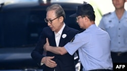 Former South Korean president Lee Myung-bak, left, is helped by a prison official as he arrives at a court to attend his trial in Seoul, Sept. 6, 2018.