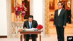 Cambodian Prime Minister Hun Sen signs on to a guest book as his Thai counterpart stands at Government House in Bangkok, Thailand, Friday, Dec. 18, 2015. (Athit Perawongmetha/Pool Photo via AP)