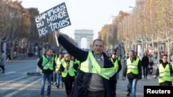 A man wearing a yellow vest, a symbol of French drivers' protest against higher fuel prices, holds a placard with the message, "World Champions in Taxes," as demonstrators gather on the Champs Elysees in Paris, France, Nov. 17, 2018. 