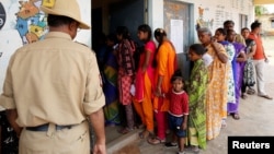 A policeman stands guard as voters wait to cast their ballot outside a polling station during Karnataka assembly elections at a village on the outskirts of Bengaluru, India, May 12, 2018.