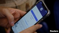 Seorang pengguna Facebook login di ponselnya di sebuah kafe,19 November 2020. Pegawai Komisi Penyiaran Indonesia (KPI) berinisial MS yang menjadi korban pelecehan seksual meminta warganet untuk tidak berkomentar negatif terhadap keluarga pelaku. (Foto: REUTERS/Kham)
