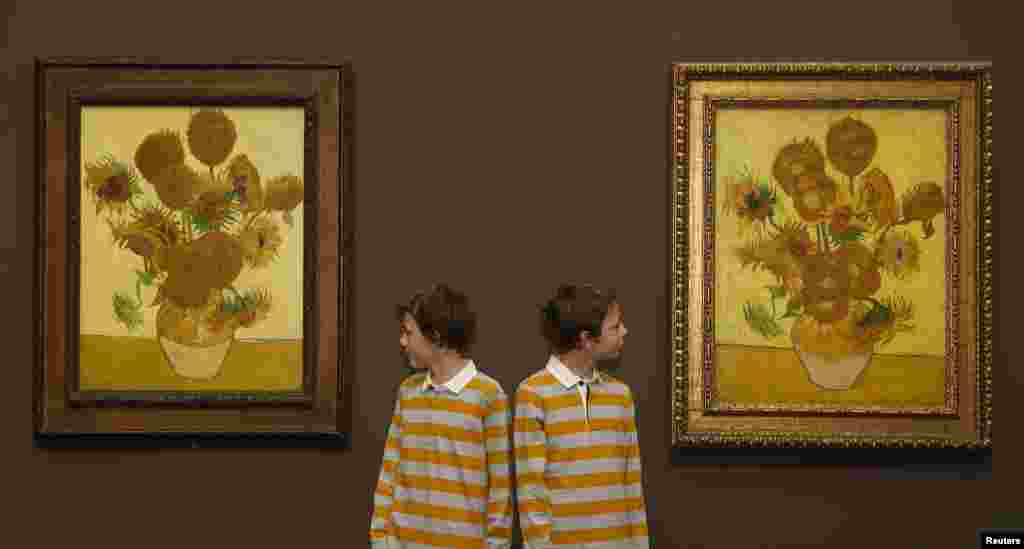 Twins Edgar (L) and Gabriel pose for photographers between Vincent van Gogh&#39;s paintings Sunflowers,1888 (L) and Sunflowers, 1889 at the National Gallery in London. The two paintings have been reunited in London for the first time in 65 years and will be on display for three months from Jan. 25. 
