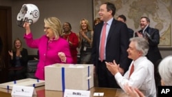 Secretary of State Hillary Rodham Clinton holding up a football helmet presented to her as she returned to work after a month-long absence caused first by a stomach virus, then a fall and a concussion, and finally a brief hospitalization for a blot clot n